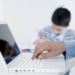 Boy doing homework while his father using laptop