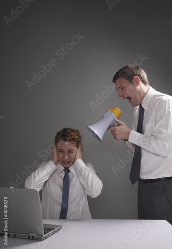 Photo: Businessman screaming through a megaphone, businesswoman covering her ears Businessman screaming through a megaphone, businesswoman covering her ears