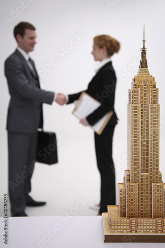 Photo: Model of Empire State Building, business people shaking hands in the background Model of Empire State Building, business people shaking hands in the background