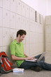 Man using laptop while leaning against lockers