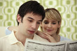 Man reading newspaper, woman watching