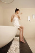Woman sitting at the edge of bathtub smelling body spray on her wrist