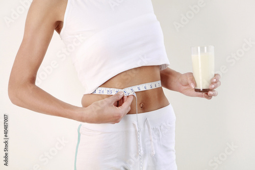 Photo: Woman with measuring tape around her waist holding a glass of milk Woman with measuring tape around her waist holding a glass of milk