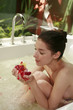 Woman in bathtub playing with flower petals
