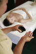Woman lying on massage table, massage therapist pouring oil on palm