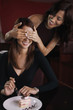 Woman covering her friend's eyes while her friend is eating cake