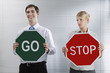 Foto: Businessman with a 'Go' sign smiling, businesswoman with a 'Stop' sign staring at him annoyingly Businessman with a 'Go' sign smiling, businesswoman with a 'Stop' sign staring at him annoyingly