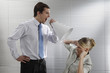 Foto: Businessman screaming through megaphone, businesswoman covering her ears Businessman screaming through megaphone, businesswoman covering her ears