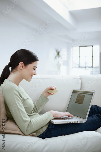 Photo: Woman looking at credit card while using laptop Woman looking at credit card while using laptop