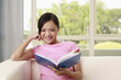 Photo: Woman sitting on the couch reading book, smiling Woman sitting on the couch reading book, smiling