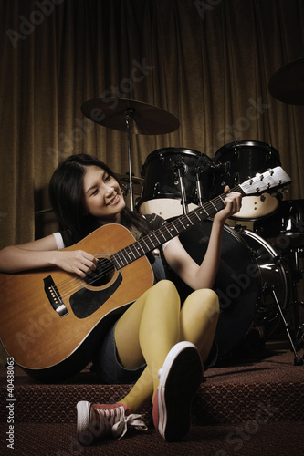 Photo: Young woman smiling while playing guitar Young woman smiling while playing guitar