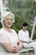 Foto: Senior woman folding her arms while smiling at the camera, woman reading book in the background Senior woman folding her arms while smiling at the camera, woman reading book in the background