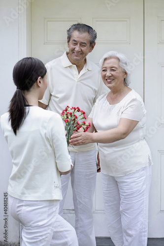 Photo: Woman giving senior woman a bouquet of flowers, senior man smiling while watching Woman giving senior woman a bouquet of flowers, senior man smiling while watching