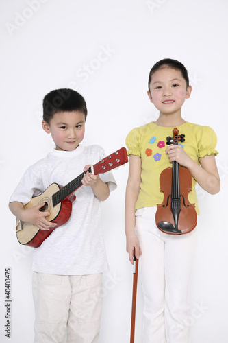 Photo: Boy playing guitar while girl is holding a violin Boy playing guitar while girl is holding a violin