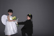 Boy with tuxedo and devil horns giving flowers to girl wearing white dress and angel wings