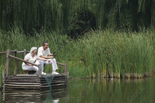 Photo: Senior couple sitting on a dock fishing Senior couple sitting on a dock fishing
