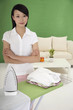 Woman standing next to ironing board and ironed clothes with her arms folded