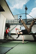 Photo: Young woman doing a breakdance move, young man with headphones using laptop in the background Young woman doing a breakdance move, young man with headphones using laptop in the background