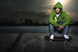 Man in green hooded sweater sitting on sidewalk, stepping on skateboard