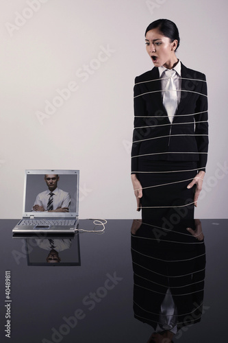 Foto: Businesswoman tied up with rope connected to laptop Businesswoman tied up with rope connected to laptop