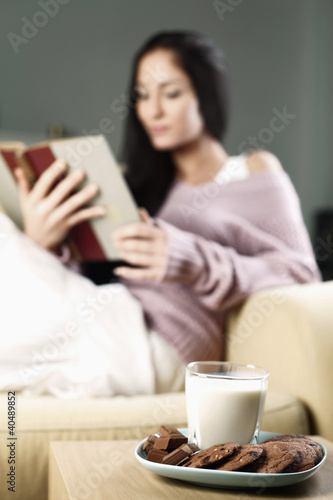 Photo: Chocolate, cookies and a glass of milk, woman reading in the background Chocolate, cookies and a glass of milk, woman reading in the background