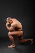 Undressed tanned bodybuilder stands on one knee and thinks