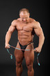 Undressed tanned bodybuilder holds measuring tape and looks down