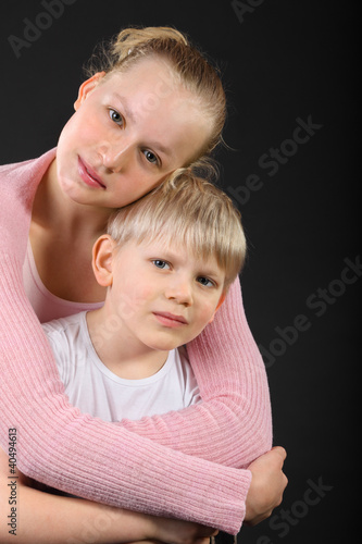 Foto: Little brother and beautiful sister embrace on black background Little brother and beautiful sister embrace on black background