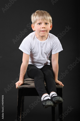 Photo: Little blond boy pull on his hands at old stool in black studio Little blond boy pull on his hands at old stool in black studio