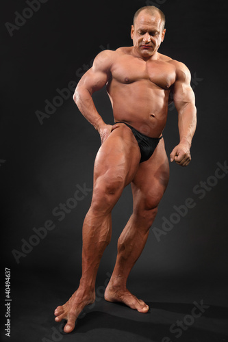 Photo: Undressed tanned bodybuilder touches floor by toe Undressed tanned bodybuilder touches floor by toe