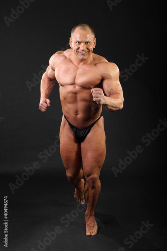 Photo: Undressed sunburnt smiling bodybuilder runs inside black studio Undressed sunburnt smiling bodybuilder runs inside black studio