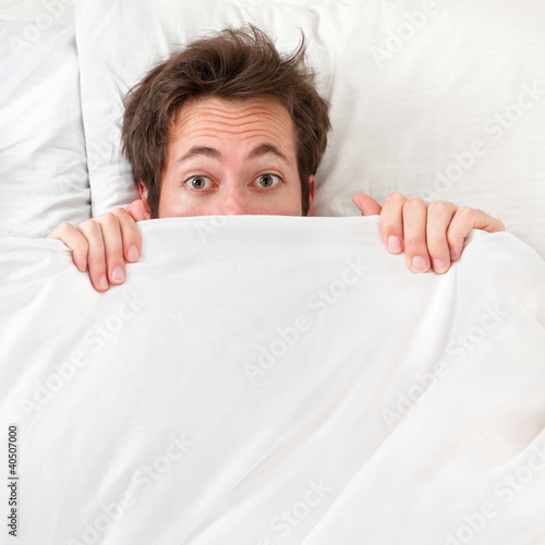 Photo: Scared man hiding in bed Scared man hiding in bed