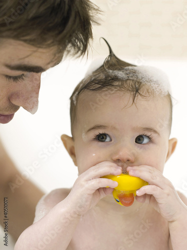 Photo: Baby girl playing with toy while her father bathing for her Baby girl playing with toy while her father bathing for her
