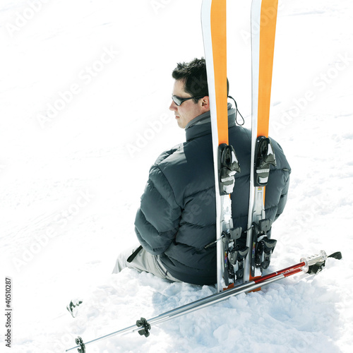 Photo: Male skier sitting with his skis and ski poles Male skier sitting with his skis and ski poles