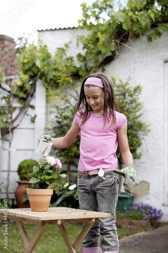 Photo: Girl with gardening gloves watering a pot of flowers Girl with gardening gloves watering a pot of flowers