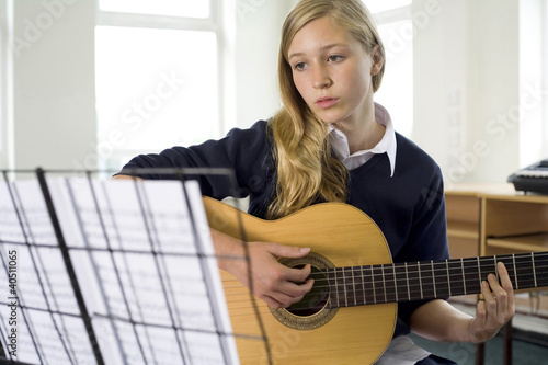 Photo: Girl plucking guitar in music room Girl plucking guitar in music room