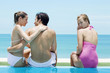 Man and two women sitting at the swimming pool