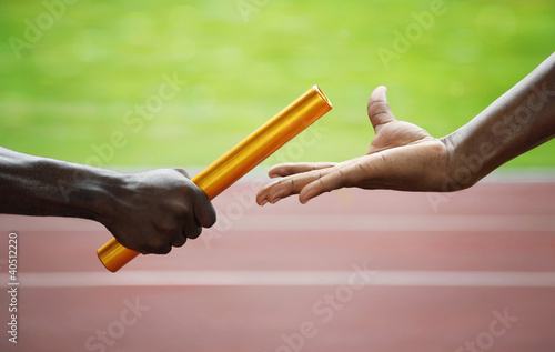 Photo: Two men passing golden baton in stadium Two men passing golden baton in stadium