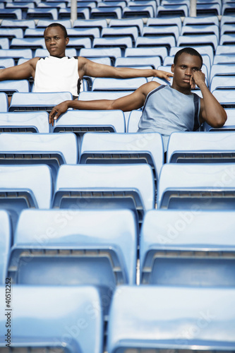 Photo: Men sitting amongst rows of blue seats in stadium Men sitting amongst rows of blue seats in stadium