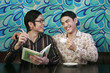 Man holding diary and pen with his guy friend sitting next to him drinking coffee
