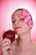 Woman with flower petals decorating her face, posing with a red apple