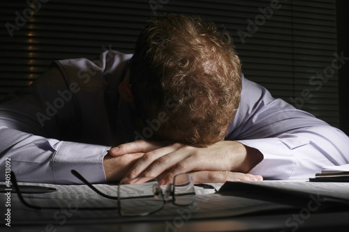 Photo: Distraught businessman with his head on the table, covering his face Distraught businessman with his head on the table, covering his face