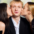 Foto: Two young attractive women kissing man, outdoors Two young attractive women kissing man, outdoors