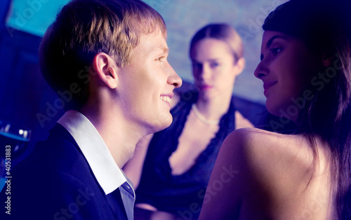Foto: Young couple and woman looking at them at club Young couple and woman looking at them at club