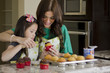 Young mother decorating cupcakes with daughter