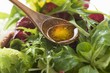 Olive oil in wooden spoon above salad leaves