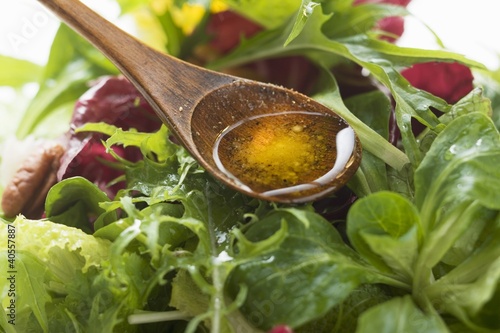 Foto: Olive oil in wooden spoon above salad leaves Olive oil in wooden spoon above salad leaves