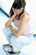 Young woman, squatting on scales, looking down