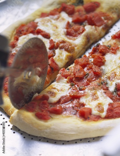 Photo: Cutting tomato and mozzarella pizza with pizza cutter Cutting tomato and mozzarella pizza with pizza cutter