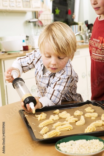 Photo: Boy piping biscuit dough onto baking tray with biscuit syringe Boy piping biscuit dough onto baking tray with biscuit syringe